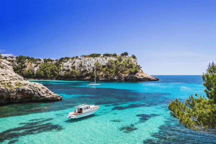 Kis motoros csónak horgonyoz a Cala Galdana öböl kristálytiszta, türkizkék vizében Menorca szigetén, Spanyolország.