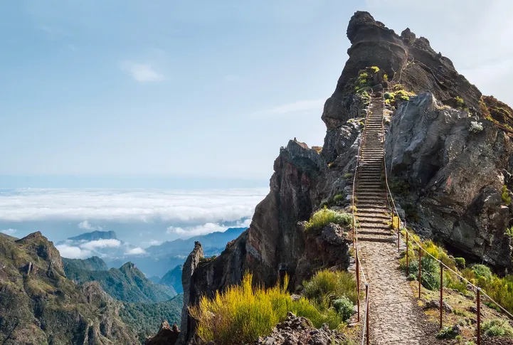 Kőlépcsős túraútvonal a madeirai Pico do Arieiro csúcsa felé, a háttérben felhőtengerrel és hegyekkel.