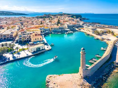 Légi felvétel Rethymno velencei kikötőjéről, a világítótoronyról és a kék tengeren haladó motorcsónakról.