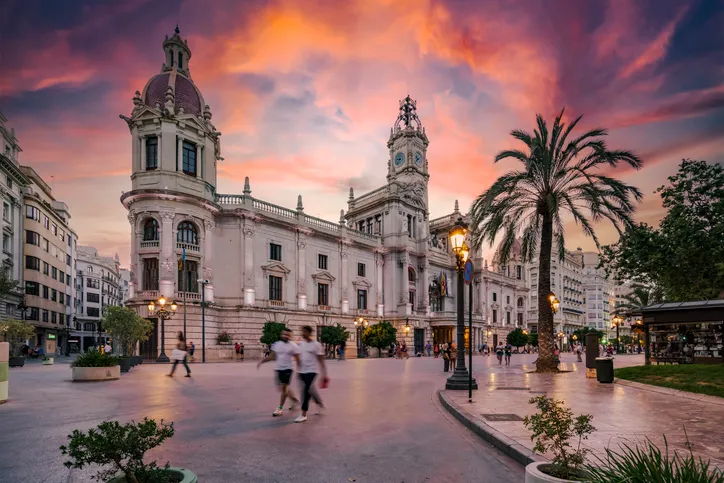 A valenciai városháza (Ayuntamiento de Valencia) kivilágított épülete a Plaza del Ayuntamientón, színes esti naplemente idején.